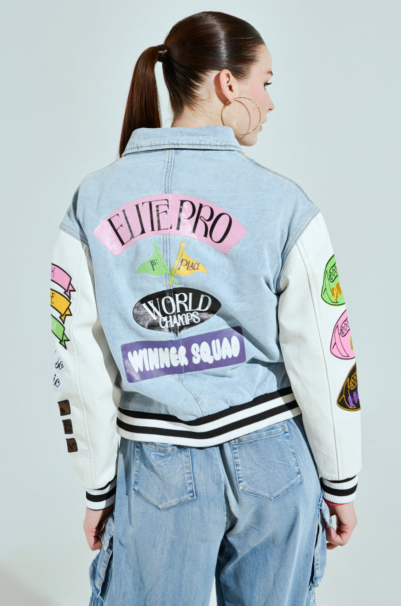 Sporting an oversized ACADEMIA DENIM BOMBER jacket with "ELITE PRO," "WORLD CHAMPS," and "WINNER SQUAD" patches, the person stands back to the camera. Paired with blue cargo pants, their unique style is completed by wearing their hair up.