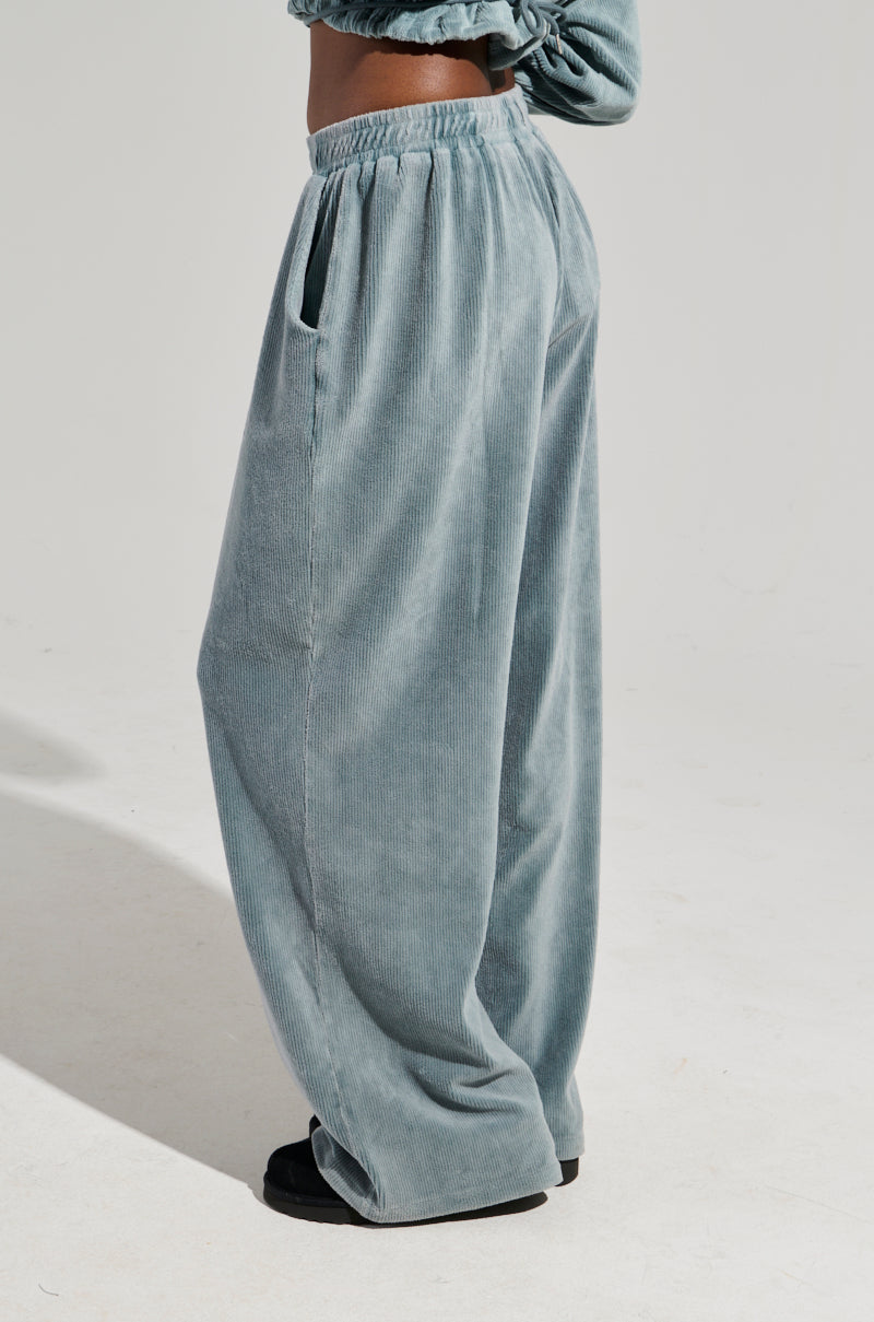 A person wearing gray FREYA SWEATPANTS and black shoes stands against a plain background, showcasing only the lower half of the body. These sweatpants are highlighted by their soft texture and convenient side pockets.