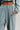 A person wearing the FREYA SWEATPANTS from AKIRA Label in a light green velour texture casually places their hand in the pocket. This look includes high-rise sweatpants with an elastic waistband paired with a cropped top, set against a plain, neutral background.