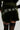 A person wearing the BRAT RHINESTONE VELVET SHORT in dark green, featuring "BRAT" rhinestone embellishments on the back. The outfit is paired with thigh-high stockings.