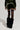 A person wearing BRAT RHINESTONE VELVET SHORTS in a green velvet material, paired with rhinestone-embellished thigh-high sheer stockings and black furry boots, is shown from behind against a plain background.