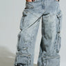 A person is wearing the "PLACES TO BE RELAXED CARGO DENIM JEANS," featuring a baggy fit, multiple pockets, and distressed detailing with drawstrings and a mid-rise design. Paired with a yellow cropped top, these jeans boast a worn, faded appearance and are complemented by white sneakers to complete the outfit.