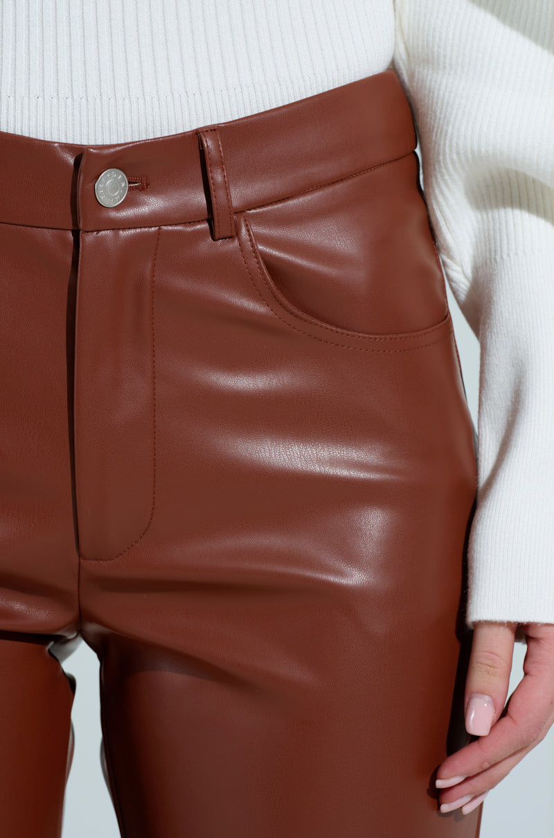 A person is wearing SAMANTHA FAUX LEATHER CAPRI PANTS IN BROWN with a white ribbed sweater. The photo highlights the waistband, silver button, and front pockets of the pants, with the person's hand slightly visible on the right side.