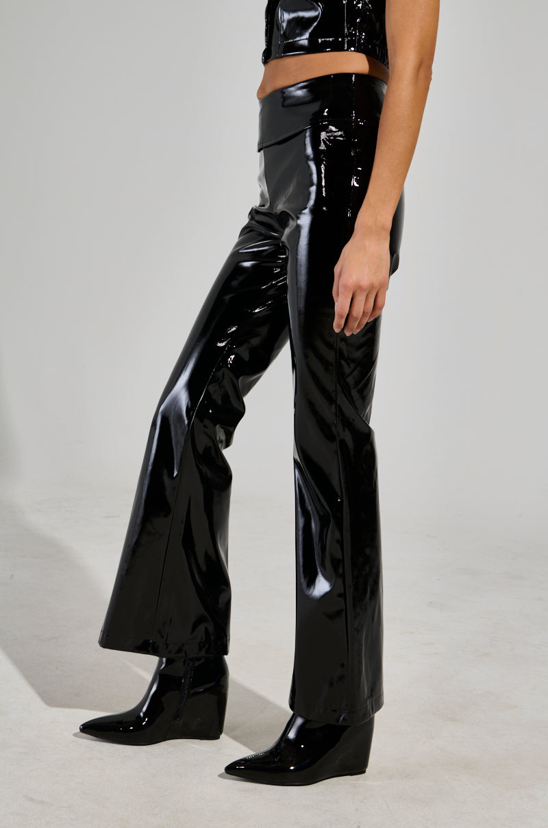 Dressed in the SEXY FOX PANT, a person pairs these patent vinyl pants with black pointy-toed shoes, radiating a sleek and seductive vibe against a light gray backdrop. The side view highlights the glossy appeal from the midriff down.