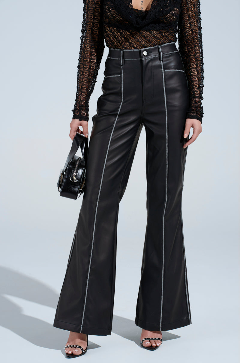 Wearing FLY GIRL FAUX LEATHER PANT with white stitching, a sheer black long-sleeve top, black heeled sandals, and holding a black handbag, a person stands against a plain background. 0