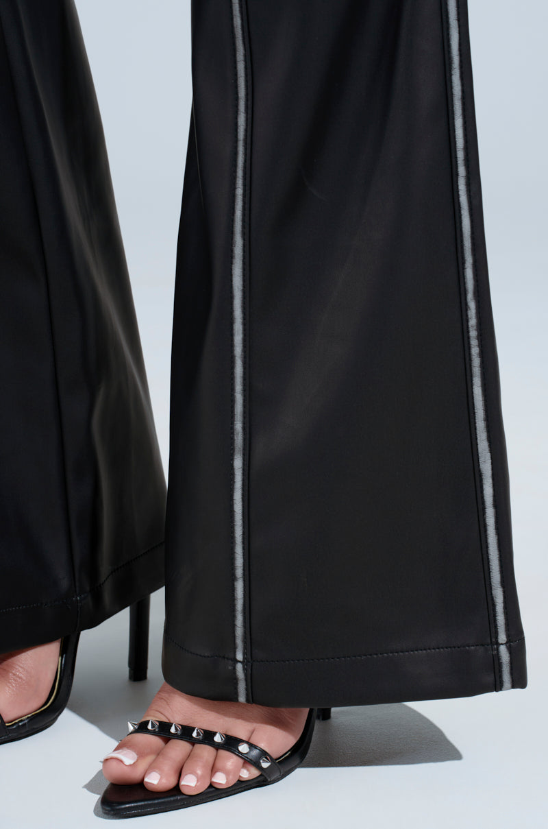 Close-up of a person wearing FLY GIRL FAUX LEATHER PANT featuring a black flared leg silhouette with visible seams, high-rise fit, and floor-grazing length, styled with open-toe black studded high heel sandals. 5