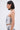 A woman with straight, shoulder-length dark hair wears the READ ME CORSET, a strapless sweetheart neckline crop top with a monochrome abstract snakeskin pattern and lace-up sides, paired with matching bottoms, hoop earrings, and a chunky chain necklace.