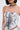 A woman wears the READ ME CORSET, a strapless design with a sweetheart neckline, monochrome abstract print, and lace-up sides. She pairs it with a black charm pendant choker and sports a short, straight hairstyle.