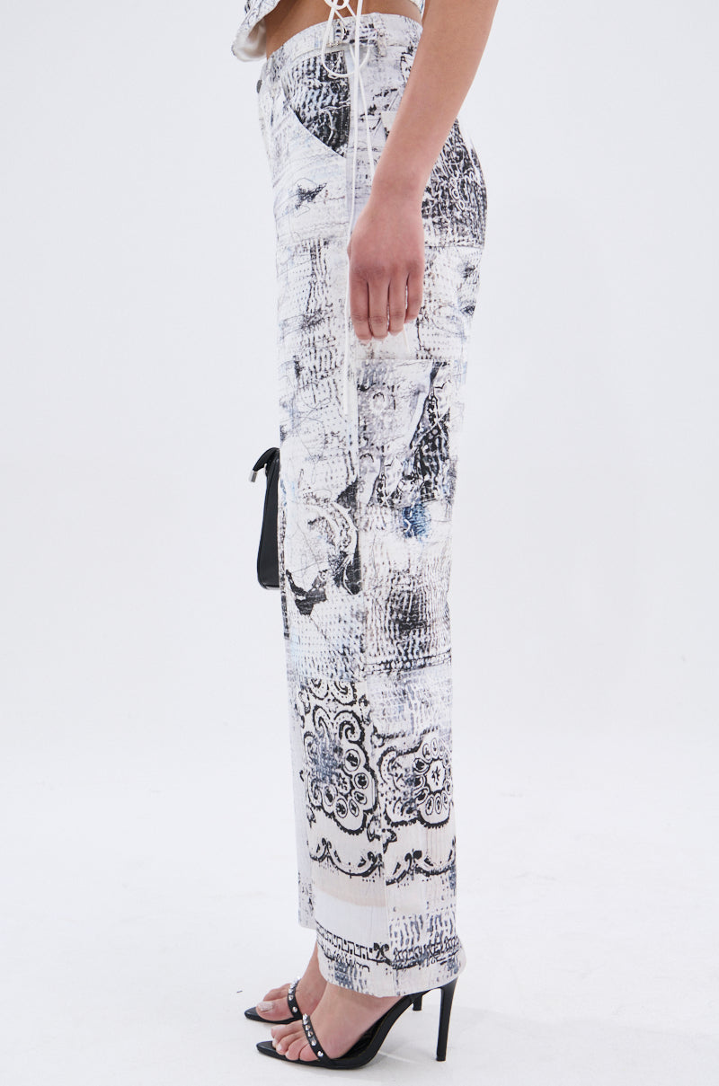 The lower half of a person is shown in profile, wearing the AKIRA Label READ ME TROUSER with an abstract linework print and black heeled sandals against a plain white background.