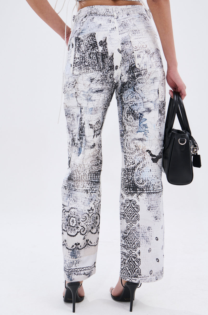 A person wearing AKIRA Label's high-waisted READ ME TROUSER in white with abstract linework, holding a black handbag and standing in black heels, photographed from the back against a plain background.