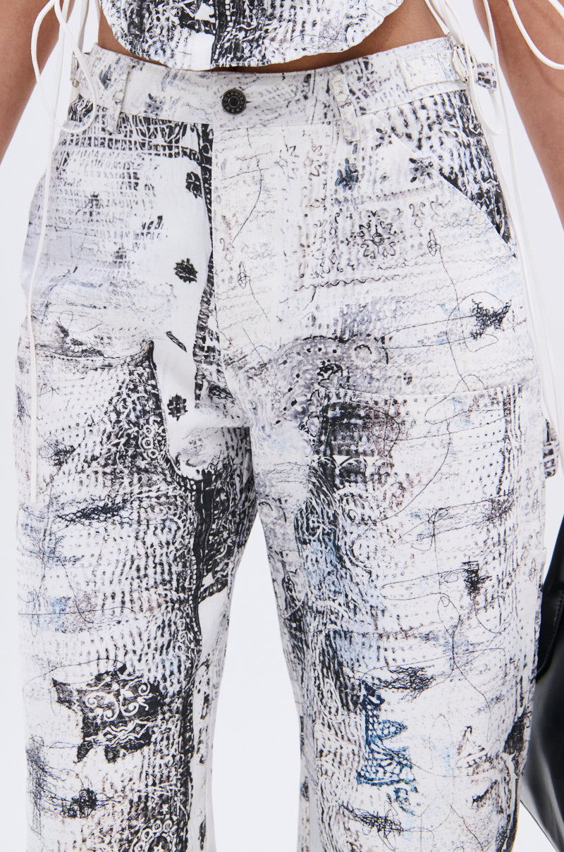 Close-up of a person wearing the READ ME TROUSER by AKIRA Label—white pants with an abstract black and gray linework print, high-rise fit, belt loops, pockets, and button closure. Their hand holds a black bag.
