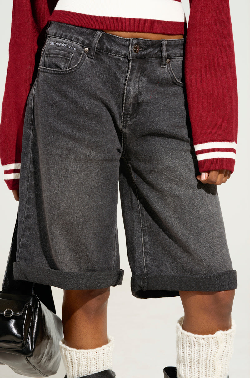 A person wearing DONT KNOW DONT CARE BERMUDA SHORT in long, wide-leg, dark denim style, paired with a red and white striped sweater and knit leg warmers. They are carrying a black handbag. The focus is on the outfit.