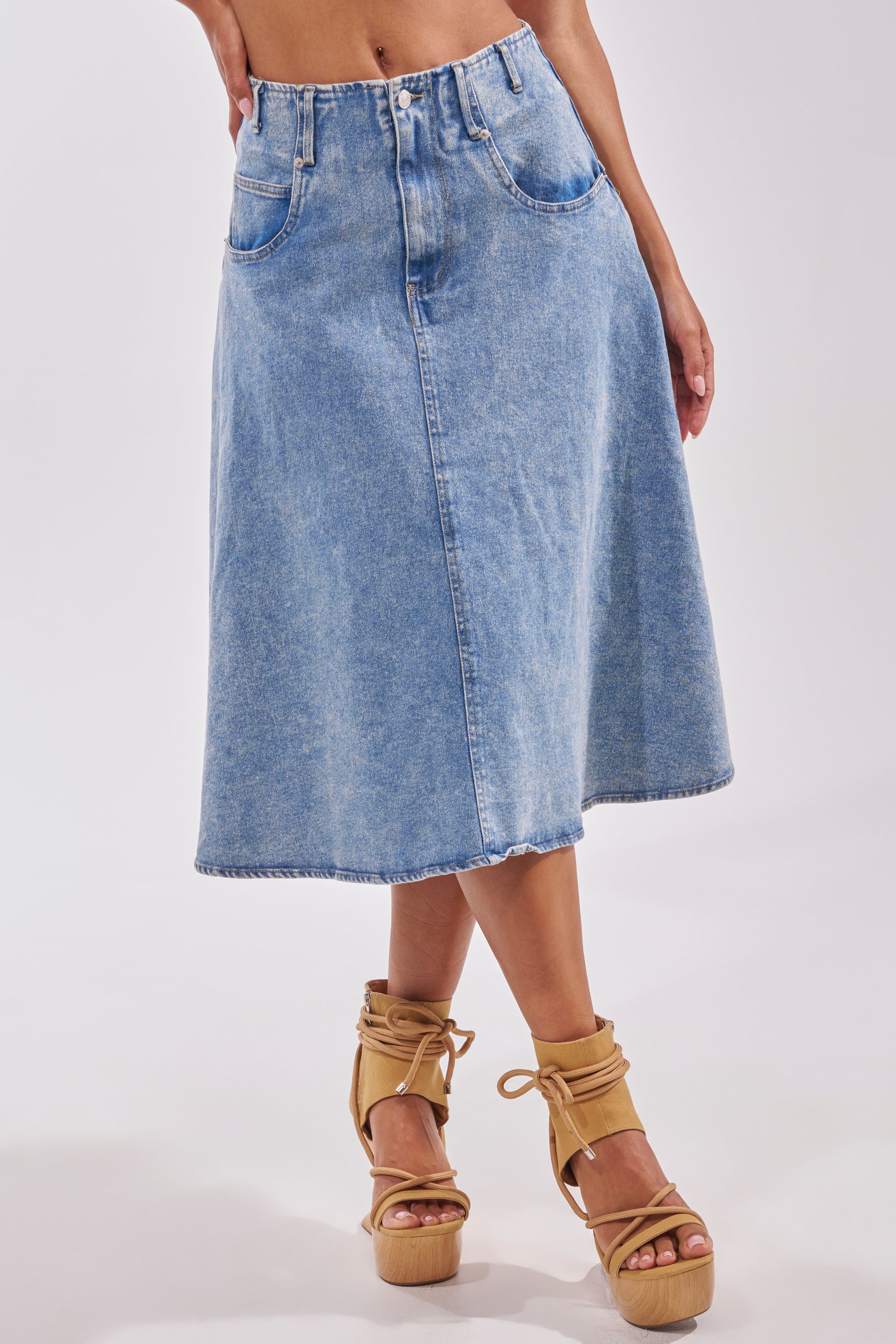 A person wears the BRITNEY MIDI DENIM SKIRT with tan platform sandals featuring ankle straps, standing against a plain light background—an ideal choice for a chic, casual streetwear look. 2