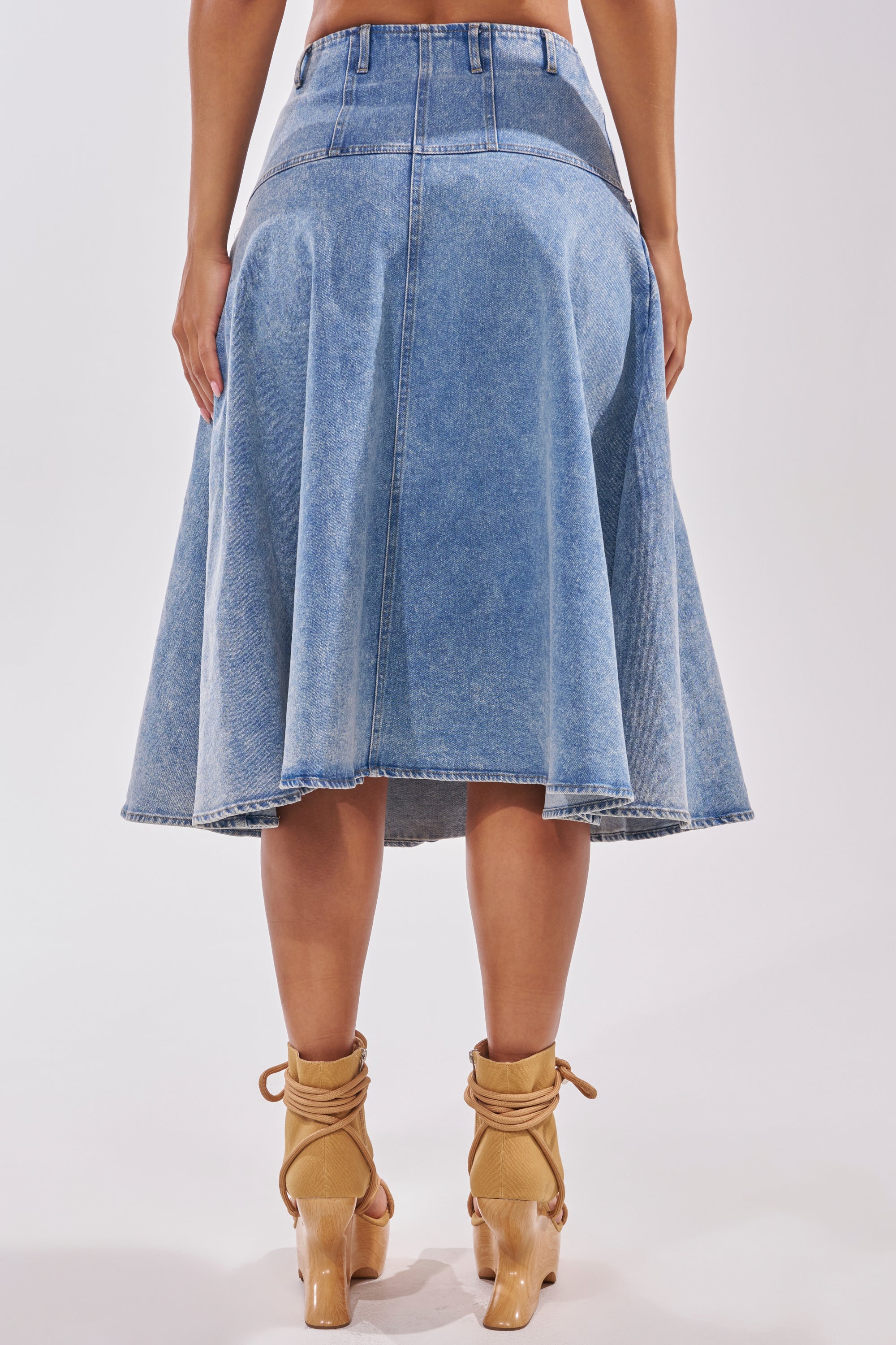 Someone models the BRITNEY MIDI DENIM SKIRT, a high-waisted, flared denim midi, paired with tan lace-up heels and shown from the back against a plain white background—ideal for casual streetwear. 4