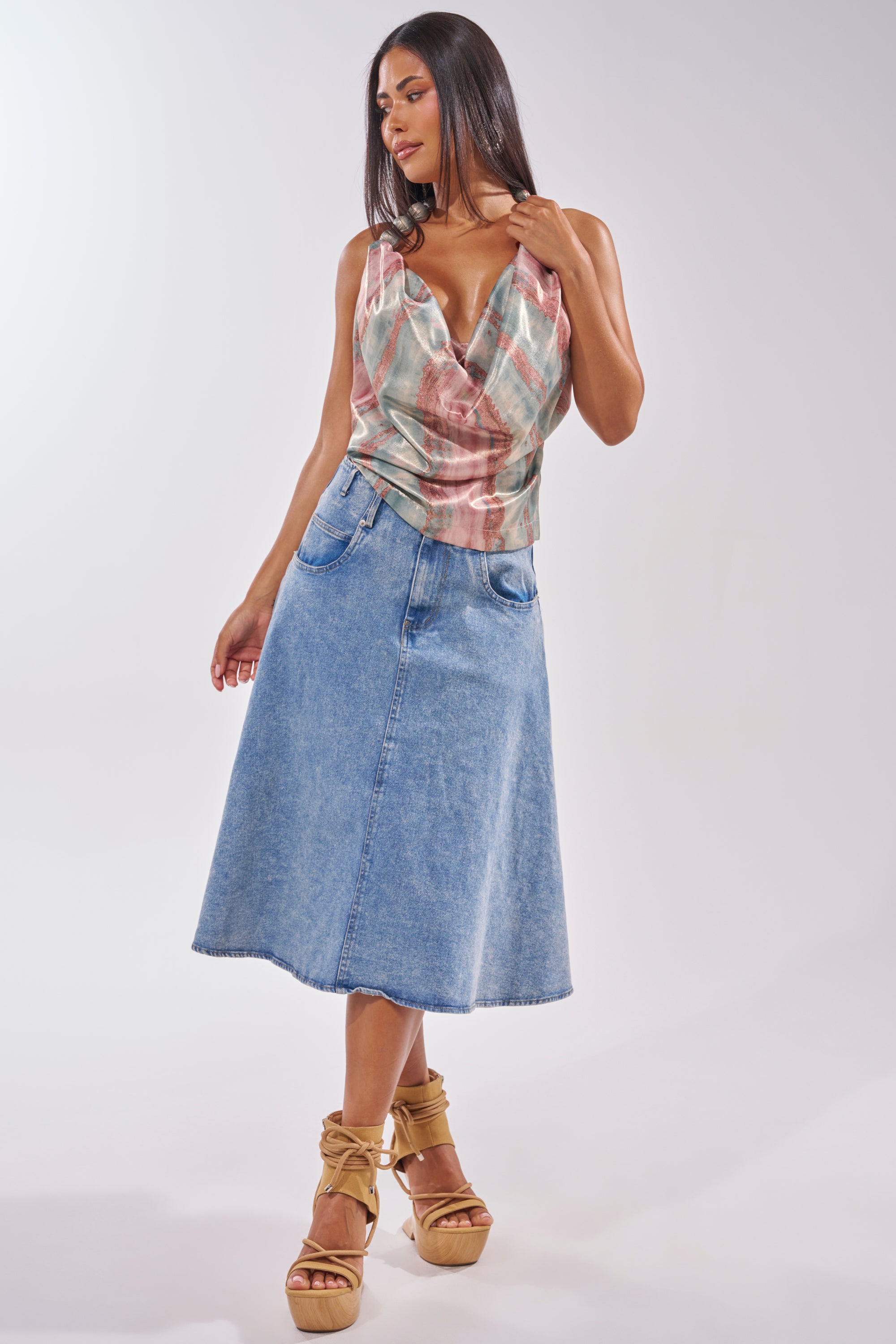 A woman with long dark hair and tan wedge sandals wears a sleeveless plaid cowl-neck top paired with the BRITNEY MIDI DENIM SKIRT, creating a relaxed, casual streetwear vibe against a simple light background. 5