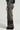 A person wearing a gray sweater and the READ MY LIPS PATCHWORK DENIM JEANS, which feature faded black fabric with fringed hems and embroidered faux leather patches on the wide-leg silhouette. The photo is taken from the side, highlighting the jeans' intricate details.