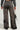 A person wearing a gray sweater and READ MY LIPS PATCHWORK DENIM JEANS, which have a wide-leg silhouette with embroidered faux leather patches, fringed hems, and display dollar signs along with other symbols on the plain background, is holding a small black handbag.