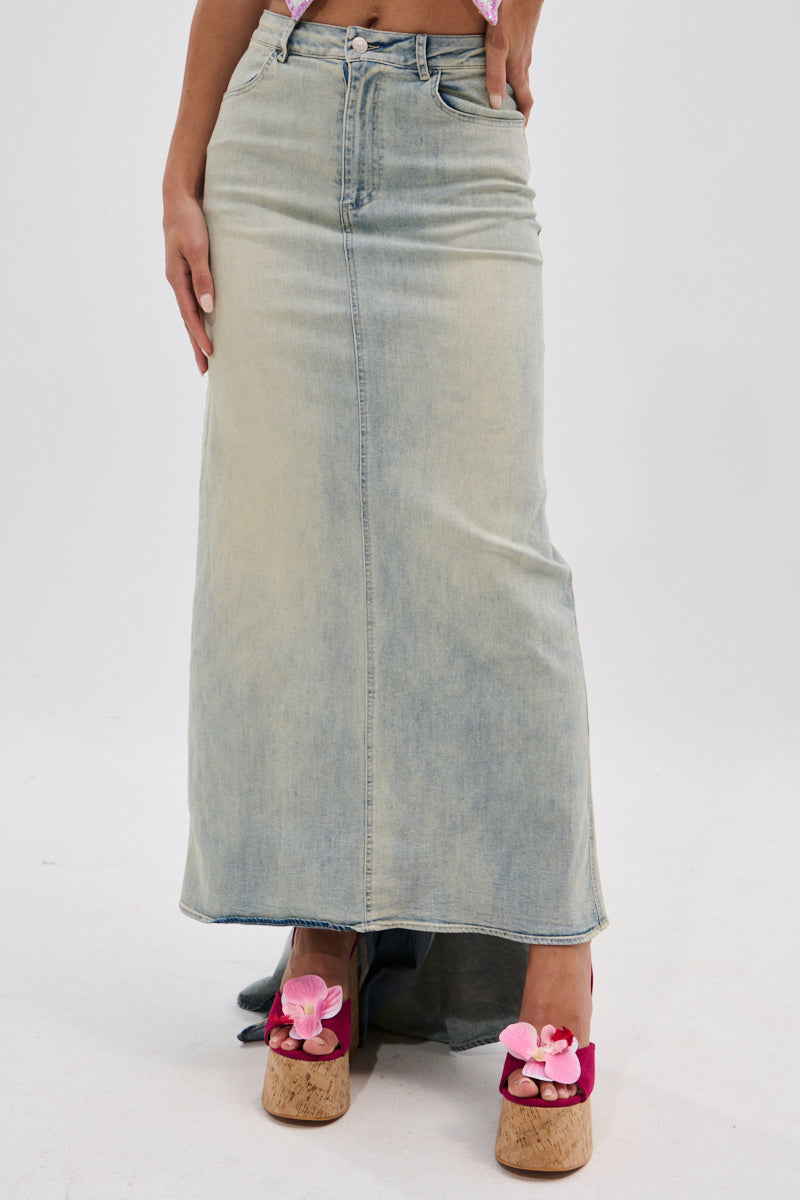 A person wearing the OH THE DRAMA BACK BOW DENIM MAXI SKIRT WITH TRAIN and cork platform sandals with pink flowers stands against a plain white background.