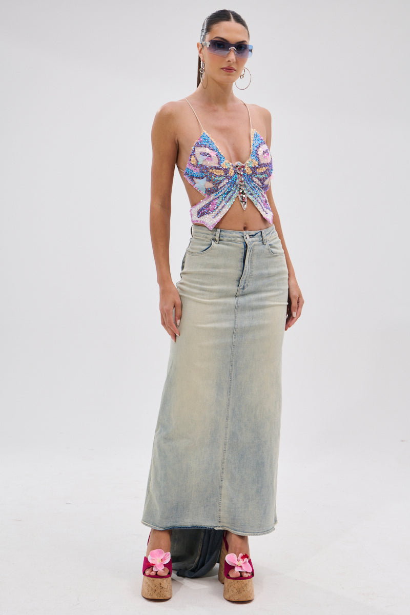 A woman wearing sunglasses, a colorful sequined bow crop top, and platform heels with pink flower details stands against a white background in the OH THE DRAMA BACK BOW DENIM MAXI SKIRT WITH TRAIN.