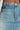 A close-up of someone in the OH THE DRAMA BACK BOW DENIM MAXI SKIRT WITH TRAIN showcases its high-rise fit, faded blue hue, detailed stitching, front button, and waistband.