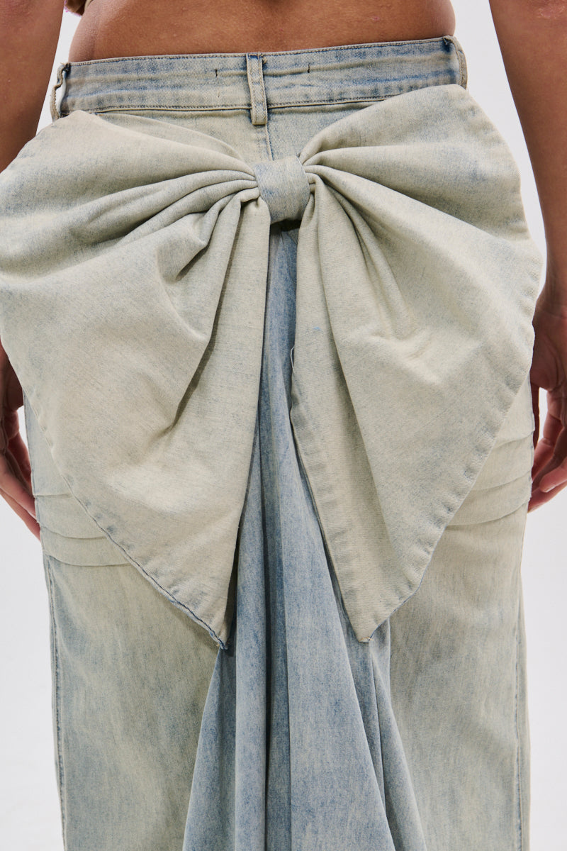Close-up of the back of a person wearing the OH THE DRAMA BACK BOW DENIM MAXI SKIRT WITH TRAIN, featuring a large decorative bow at the waistband for a striking statement look.