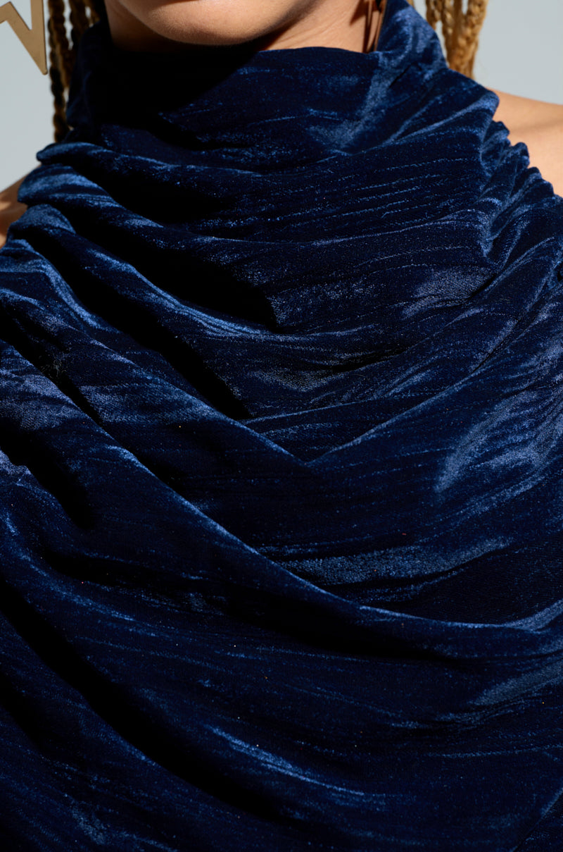 Close-up of an individual wearing the FEELING TEMPTED HALTER NECK TIE BACK TOP in textured, deep blue crushed velvet. The fabric is elegantly draped, forming soft folds and a rich sheen. A glimpse of an earring and braided hair enhances the sophisticated look. 4