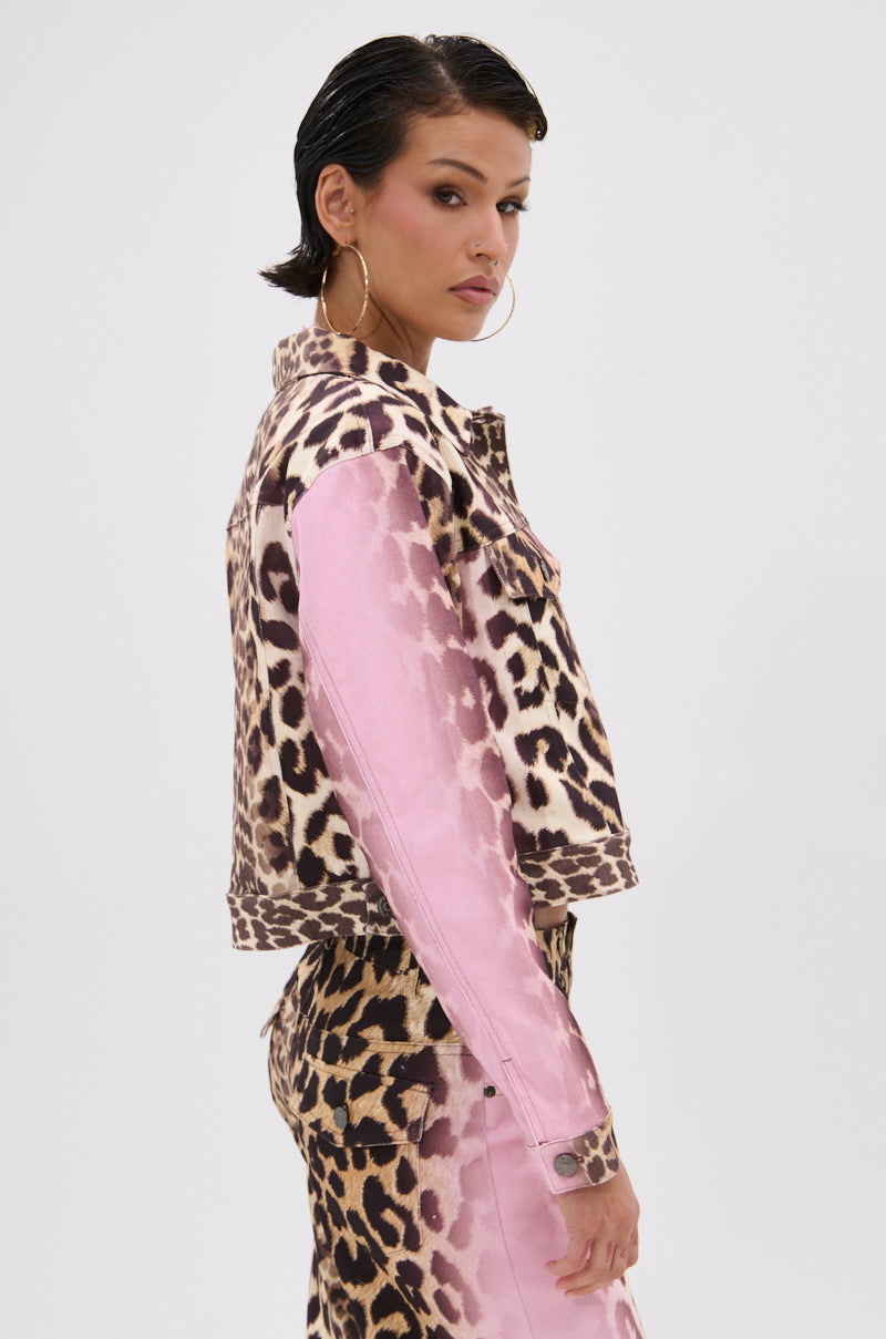 A woman with slicked-back hair wears the COCO LEOPARD PRINT DENIM JACKET in pink and leopard print, paired with matching high-waisted pants and hoop earrings, standing sideways while looking at the camera.