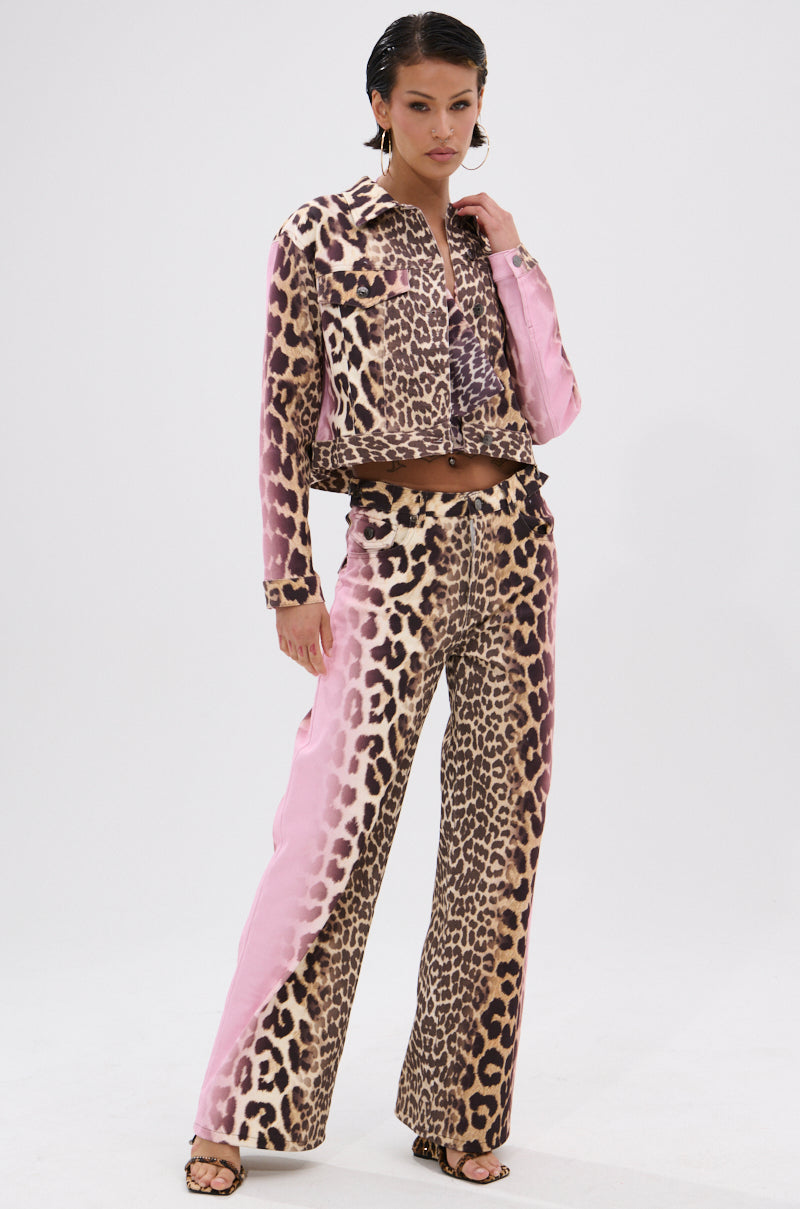 A woman stands confidently in the COCO LEOPARD PRINT DENIM JACKET, styled with slicked-back hair and wide-leg pants for a bold look against a white background.
