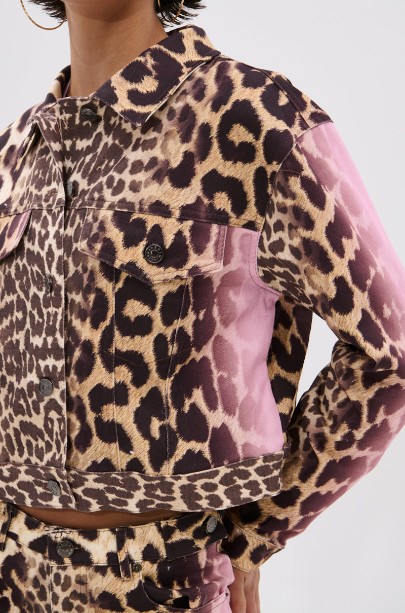 Wearing the COCO LEOPARD PRINT DENIM JACKET, a person sports a cropped silhouette with leopard print, ombre pink fade, large chest pockets, and dark buttons. Their face is partially out of frame, completing the bold look.