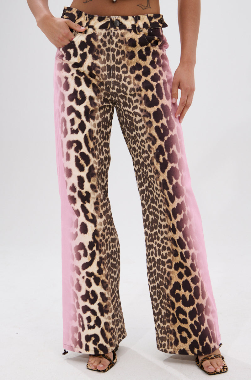 A person wears AKIRA Label COCO LEOPARD PRINT DENIM pants with pink side panels and open-toe sandals. The photo is cropped from shoulders to feet.