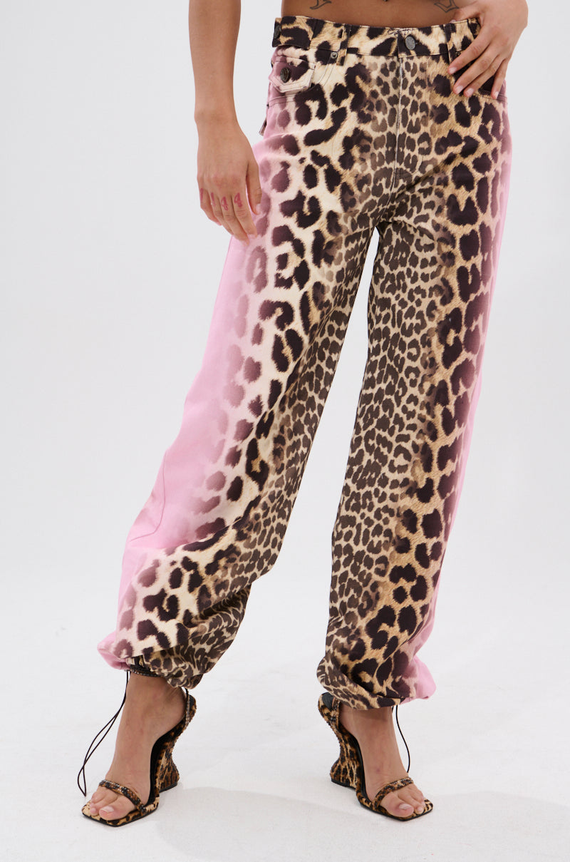 Wearing loose-fitting COCO LEOPARD PRINT DENIM pants with open-toe leopard-print heels and AKIRA Label flair, this look stands out against a plain white background.