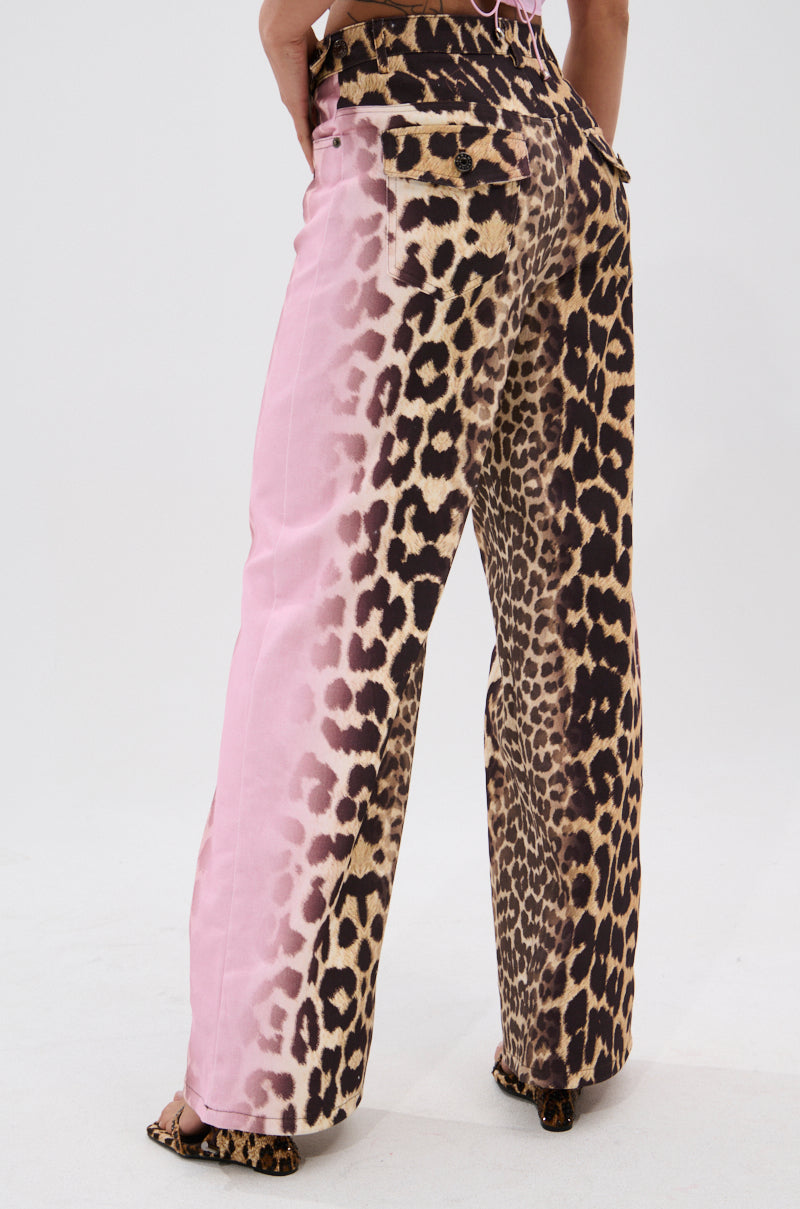 A person stands facing away, wearing high-waisted COCO LEOPARD PRINT DENIM featuring bold leopard spots, a pink gradient on one side, back pockets, and a loose straight-leg fit.