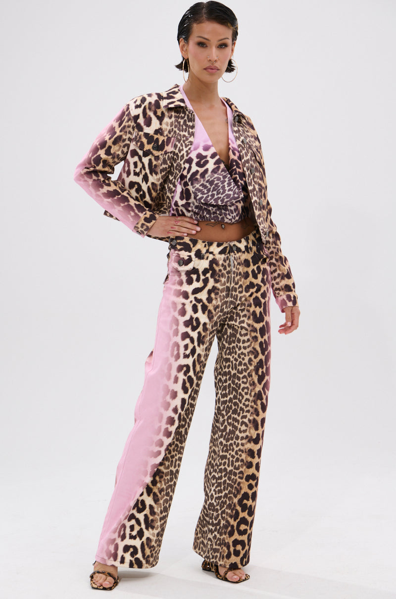 A woman stands confidently in the COCO LEOPARD PRINT DENIM set—matching jacket, wrap top, and wide-leg pants with pink color block details—paired with strappy heels against a plain white background.