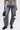 A person in JACQUELINE CUTOUT DENIM PANTS—vintage-washed gray, high-rise cutout style—paired with a gray top with sheer horizontal sleeve panels, black chunky boots, and a small black handbag.