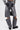 A person wears the JACQUELINE CUTOUT DENIM PANTS in vintage-washed gray with knee panels and dark back pocket patches, styled with black chunky shoes and a small black bag against a plain light background.