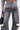 A person wears the JACQUELINE CUTOUT DENIM PANTS in vintage-washed gray with a high-rise fit, paired with a gray cropped jacket with mesh sleeve stripes and carrying a small black handbag.