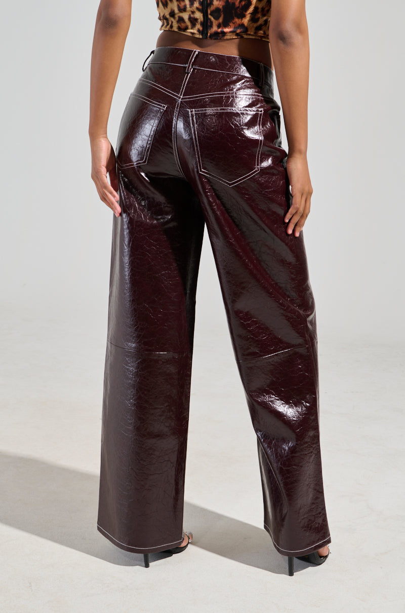 A person is wearing the "Start With Me" faux leather trousers in burgundy, paired with a leopard print top. The photo, taken from behind, showcases the trousers' high-rise fit and glossy finish along with their intricate stitching details against a plain backdrop. 3