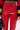 A person wearing SEXY FAUX LEATHER RED LACE-UP PANTS and a black and red long-sleeve top with yellow and white sleeve stripes, holding a black bag.