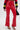 A person wears SEXY FAUX LEATHER RED LACE-UP PANTS, a black and red sports top with yellow and white stripes, black heeled sandals, holds a black handbag. The background is plain white.
