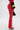 A person wearing SEXY FAUX LEATHER RED LACE-UP PANTS with side cutouts, a black and red top with yellow stripes, holding a small black bag, and strappy high-heeled sandals.