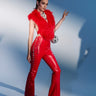 A woman poses confidently in SEXY FAUX LEATHER RED LACE-UP PANTS with high heels, a silver statement necklace, and a small bag, against a blue and white background.