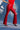 Against a blue background, only the lower body is visible, styled in eye-catching SEXY FAUX LEATHER RED LACE-UP PANTS, paired with high heels and a small silver bag.