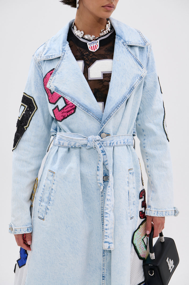 Wearing the COUNTDOWN PATCH DENIM TRENCH in light blue with varsity patches, paired with a black mesh top, chunky silver necklace, and small black bag for a sporty-chic look. 5