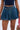 Wearing the BETTER BE DENIM MINI SKIRT in dark blue with a high-rise, flared fit, paired with a black crop top and carrying a small bag featuring a red strap and animal print. Only the lower torso and upper legs are shown.