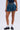 Wearing the BETTER BE DENIM MINI SKIRT in a high-rise, flared fit, paired with black loafers, white lace socks, a navy crop top, and a leopard-print bag. The photo is cropped at the midriff without showing the face.