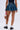 A person stands facing away, wearing the BETTER BE DENIM MINI SKIRT, black shoes with white frilly socks, and holding a small leopard-print handbag with a red strap.