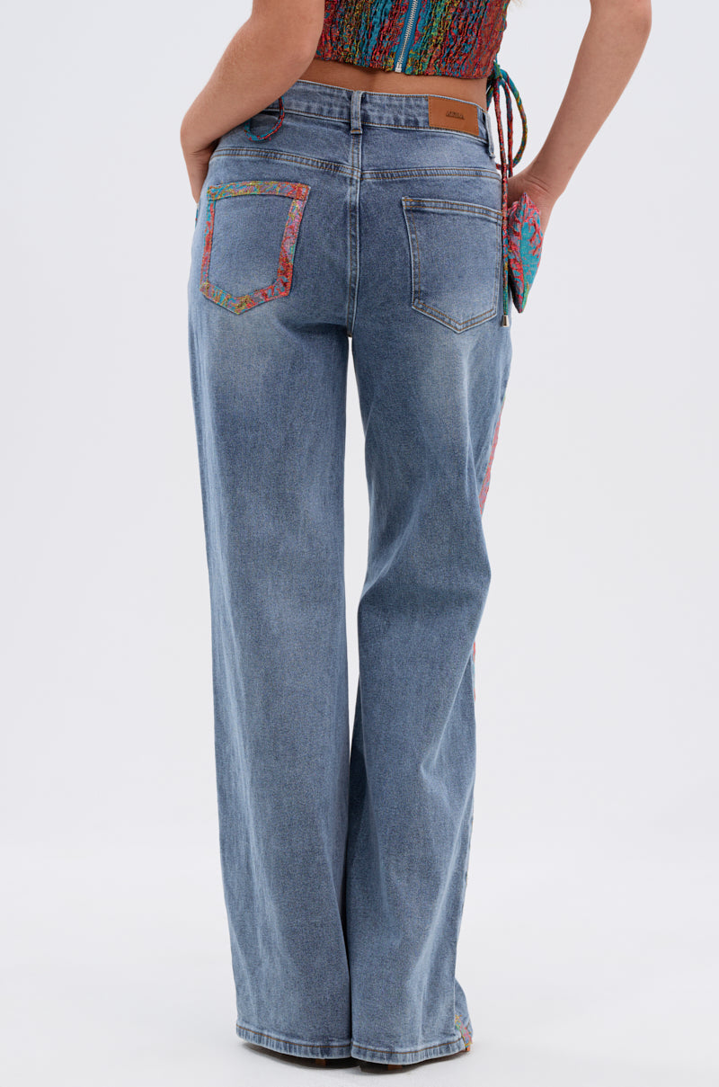 A person is seen from behind wearing PRETTY GIRL PROBLEMS DENIM WITH BOW—light blue wide-leg jeans with colorful trim on the pockets and sides—paired with a multicolored sleeveless top, set against a plain background. 5