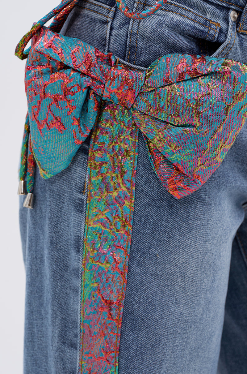 Close-up of the PRETTY GIRL PROBLEMS DENIM WITH BOW, featuring a colorful metallic bow applique and matching textured stripes in red, green, blue, and yellow near the pocket and side seam. 8