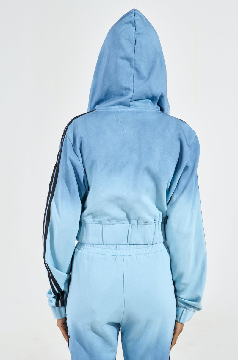 Someone is wearing the DON'T TALK TO ME I'M RUNNING ERRANDS ZIP UP SWEATSHIRT, which is light blue with black stripes on the sleeves and an ombré gradient design. The outfit includes a gathered waist on the jacket, creating a fashionable cropped silhouette as they face away from the camera.