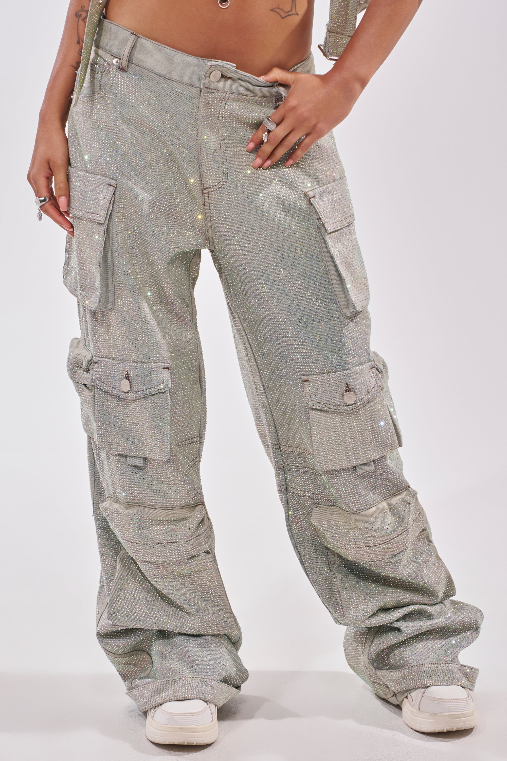 The lower torso and legs of a person wearing BLING BLING CARGO DENIM—loose-fitting, sparkly silver high-rise cargo pants with multiple pockets—are shown with white sneakers against a plain background. 1